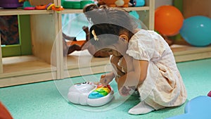 cute dark-haired girl playing with a toy in the playroom, toys on the shelves in the background full shot