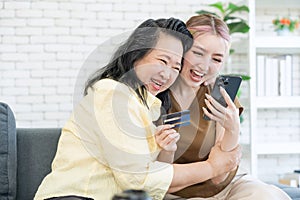 Cute daughter and elderly mom hugged each other using smartphone online shopping use credit card online at living room