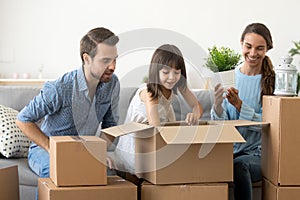 Cute daughter helping mom dad unpack boxes in new home