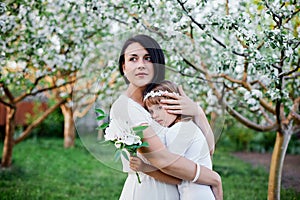 Cute daughter and mother hugging in blossom spring garden