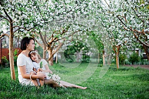 Cute daughter and mother sitting and hugging in blossom spring garden