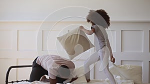 Cute daughter playing pillow fight on bed with black father