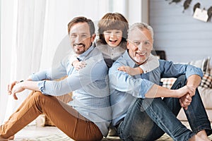 Cute delighted child hugging his father and grandfather