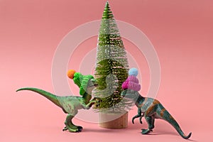 cute dinosaurs wearing knitted hats near christmas tree on a soft pink background