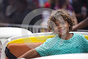 Cute diverse little boy smiling while riding an amusement park carnival ride outdoors.