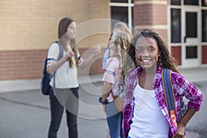 Cute, diverse pre-adolescent teen student hanging out with friends after school. Selective focus on the smiling girl student stand