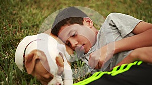 Cute dog and adorable kid laying down in grass. Puppy is eating grass