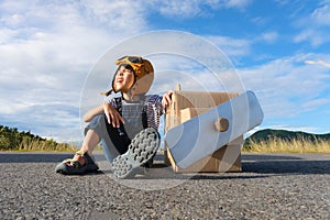 Cute dreamer little girl playing with cardboard planes on a lake road on a sunny day. Happy kid playing with cardboard plane