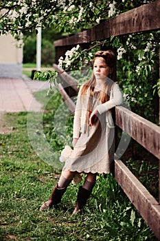 Cute dreamy child girl posing at rustic wooden fence with teddy bear