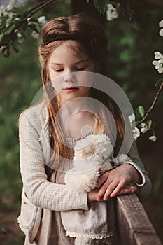 Cute dreamy child girl posing at rustic wooden fence with teddy bear