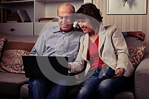 A cute elderly pair smiling and looking at a notebook