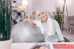 Cute elderly woman leaning on yoga ball and smiling