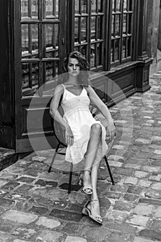 A cute, elegant girl sits on a chair in a street cafe