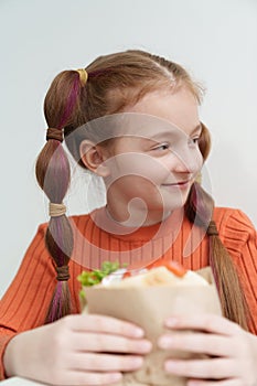 Cute elementary age girl with ponytails eating a sandwich in fast food restaurant. Adorable Ukrainian child eats pita souvlaki