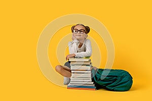 Cute Elementary School Girl Sitting At Books Stack Over Yelow Background