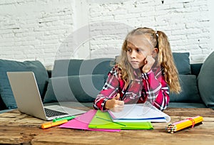 Cute elementary student feeling sad and confusing while doing difficult assignment with her laptop at home in primary school