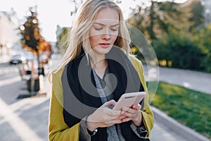 Cute emotional attractive blonde woman in coat with smartphone walks the city street. communication during the walk, lifestyle,