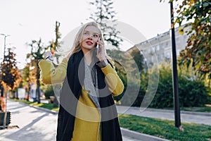 Cute emotional attractive blonde woman in coat with smartphone walks the city street. communication during the walk, lifestyle,