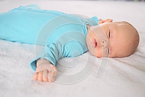 Cute emotional funny newborn infant boy in jumpsuit laying on bed. Infant baby facial expressions.
