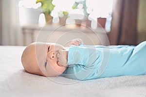 Cute emotional funny newborn infant crying boy laying on bed. Infant baby facial expressions.