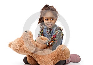 Cute ethnic girl playing with plush bear smiling