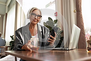 cute european gray-haired senior business woman sits in a cafe and watches a video on a laptop using headphones