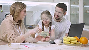 Cute excited girl holding money smiling as woman talking. Portrait of satisfied Caucasian daughter in kitchen with