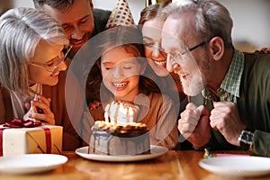 Cute excited little child making wish, blowing candles on cake while celebrating Birthday with family