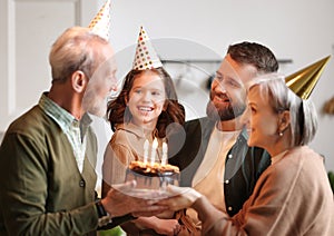 Cute excited little child making wish, blowing candles on cake while celebrating Birthday with family