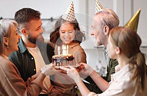 Cute excited little child making wish, blowing candles on cake while celebrating Birthday with family