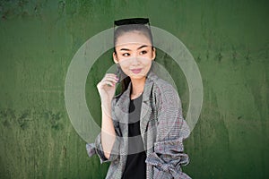 Cute exited Asian girl thinking and smiling near green wall looking to the side.