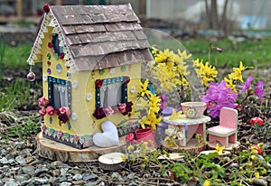 Cute fairy doll house with spring flowers outside in the garden