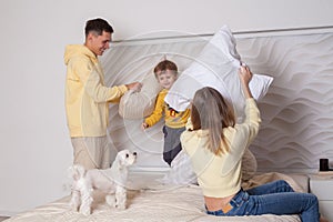 Cute family, parents with adorable child son and white litte dog playing with pillows