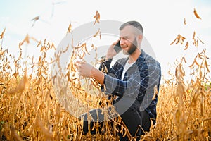 A cute farmer is standing in a soybean field and talking on the phone with his business partner