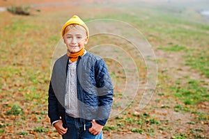 Cute fashionable boy on a walk in autumn park. Stylish kid wears trendy jacket, sweater, jeans and yellow hat. Autumn fashion,