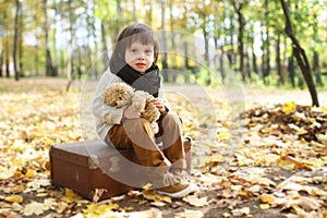 Cute fashionably dressed boy sitting on suitcase in the autumn p