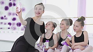 Cute Female ballet teacher is taking selfie with her little student with smartphone and posing looking at camera while