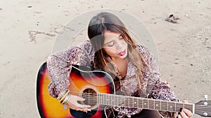 cute Female musician playing acoustic guitar on sandy beach