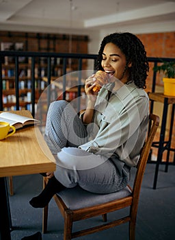 Cute female student eats croissants in cafe