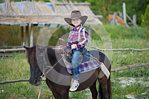 Cute fermer handsome boy cowboy in jeans enjoying summer day in village life with flowers wearing leather cow hat happyly smiling