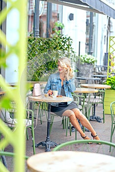A cute flirty woman, drinks coffee at a table in a street cafe.