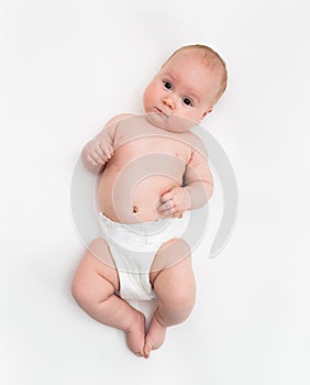 A cute four month old baby girl wearing a white diaper cover lie down on white background.