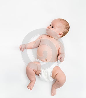 A cute four month old baby girl wearing a white diaper cover lie down on white background.