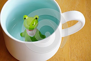 Cute frog figurine in the white mug with babyblue base