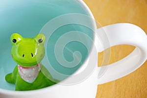 Cute frog figurine in the white mug with babyblue base