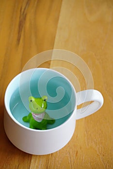 Cute frog figurine in the white mug with babyblue base