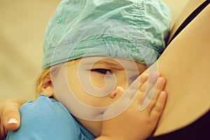 Cute frown baby boy drinks milk from mothers breast