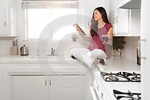 Cute fun concept of woman relaxing with a tablet in clean immaculate bright white kitchen, copy space