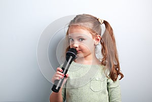 Cute fun kid girl singing song in microphone on blue background.