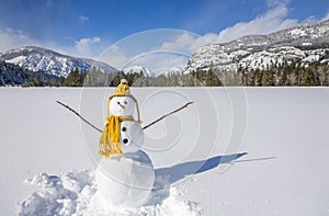 Cute fun snowman with knit hat and scarf in winter landscape snow scene with mountains and blue sky